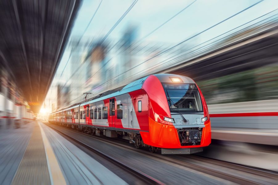 A brightly colored express train speeds past the platform in a station.