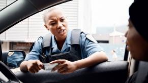 A police officer speaks to a driver and inspects their license during a traffic stop