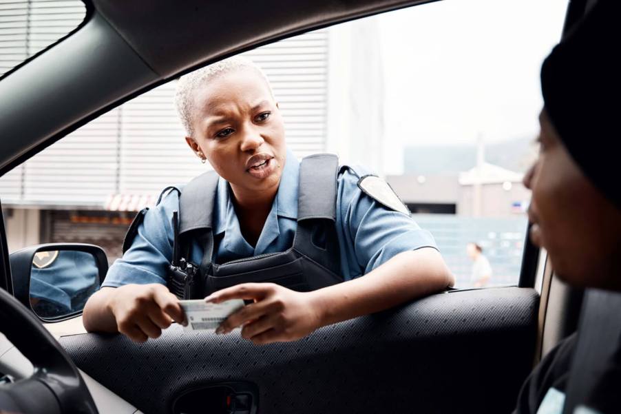 A police officer speaks to a driver and inspects their license during a traffic stop