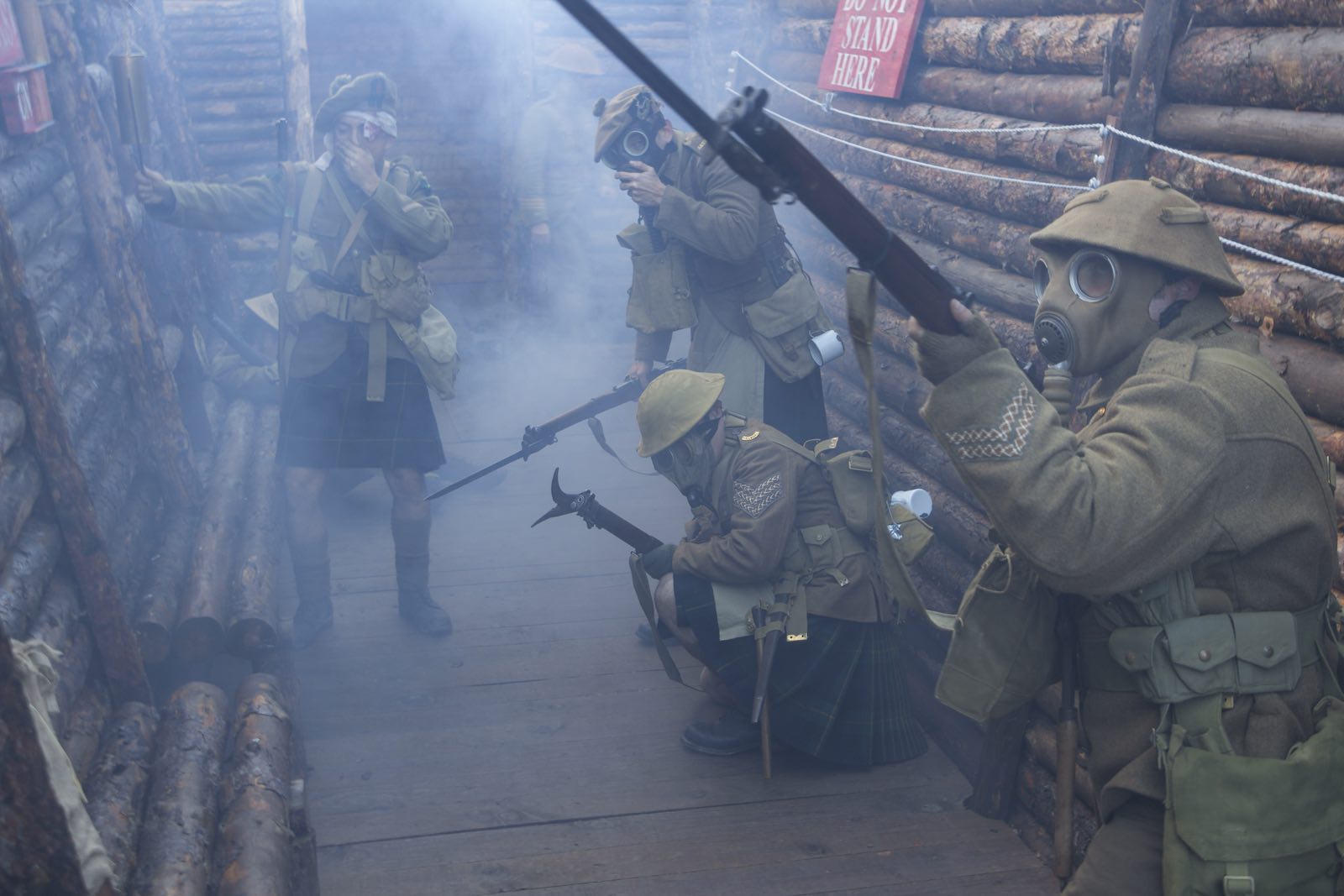 Group of WWI reenactors wearing gas masks hold guns in a trench.