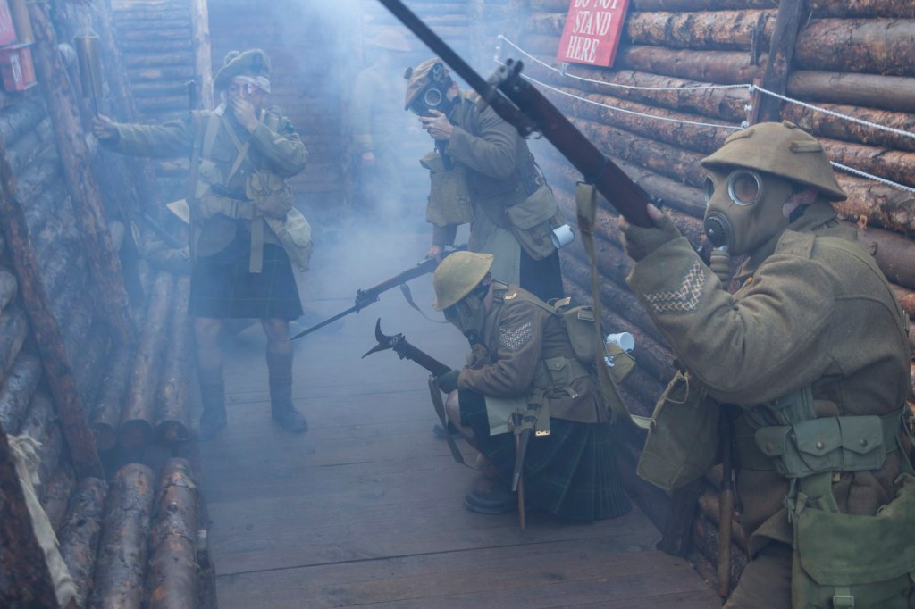 Group of WWI reenactors wearing gas masks hold guns in a trench.