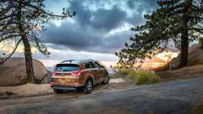 A copper-colored 2018 Kia Sportage parked on a sandy paved hill overlooking a sunset, in 2024 car insurance companies are still blacklisting certain Kias