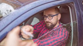 A driver hands over their driver's license to a police officer after rolling the car window down halfway.