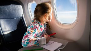 Kid looking out the window of an airplane while drawing a picture.