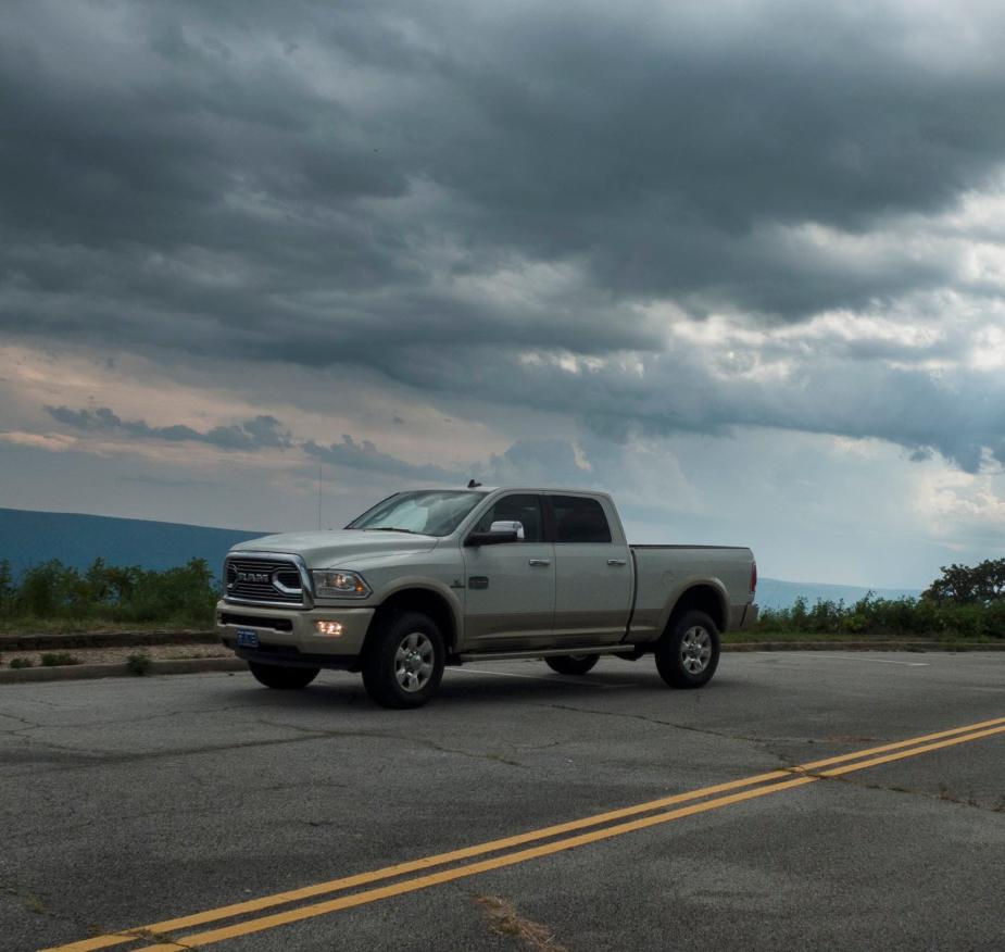 Heavy-duty Ram pickup truck with a Cummins engine parked on a mountain road, dark clouds visible in the background.