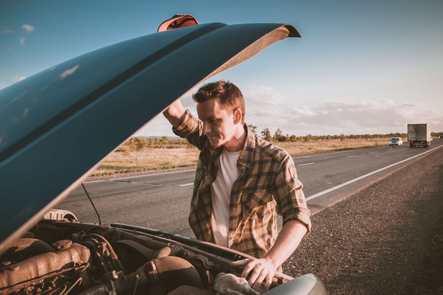 Man looks under the hood of his pickup truck parked by the highway.