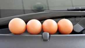 Four brown eggs on a car windshield cowl in close view egging a car causes expensive damage