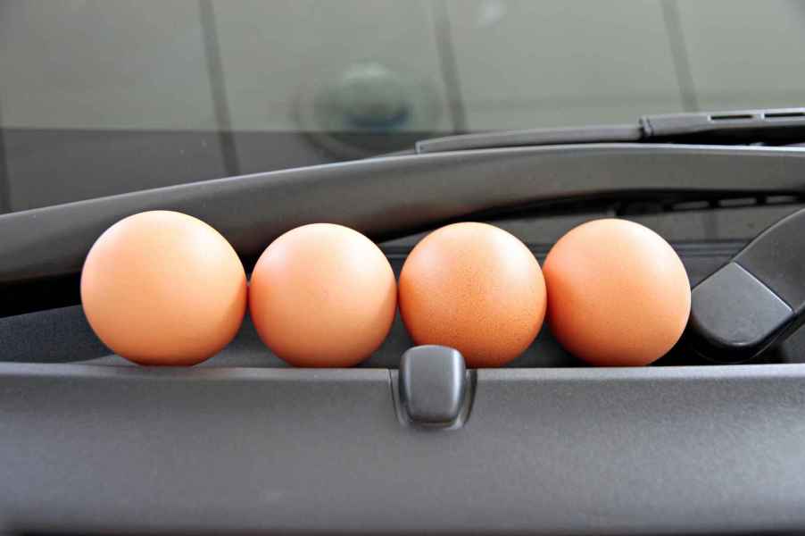 Four brown eggs on a car windshield cowl in close view egging a car causes expensive damage