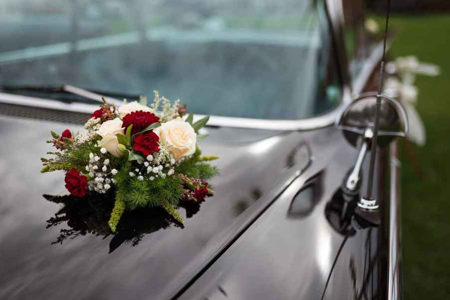 Depiction of a black funeral procession car with flowers on the hood in close view