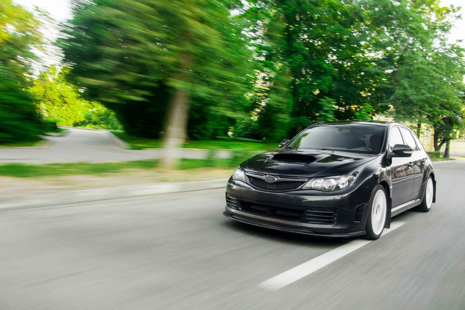 A black Subaru WRX Impreza driving fast with blurred green trees on the side of the road
