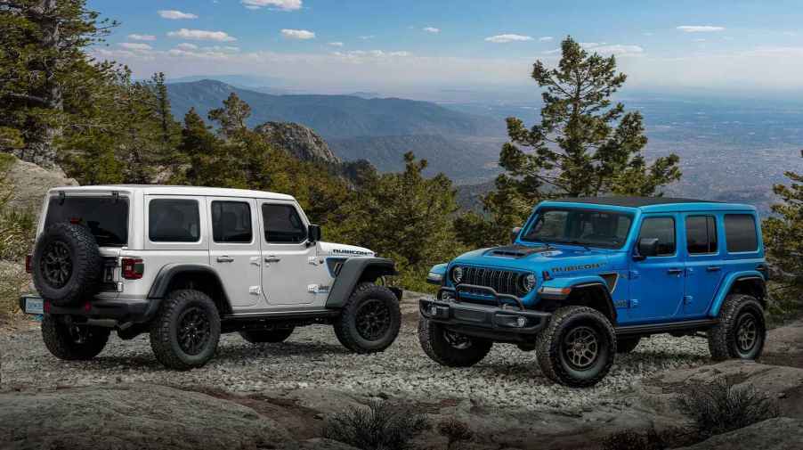 Two 2023 Jeep Wrangler SUVs parked on a gravel mountain trail facing each other in profile view