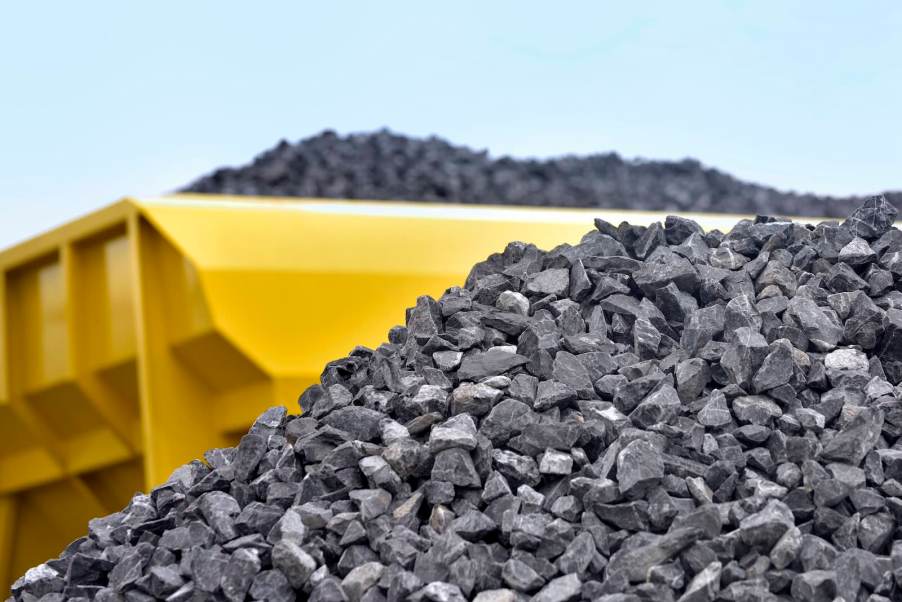 Yellow dump truck leaves a load of gravel on the ground.