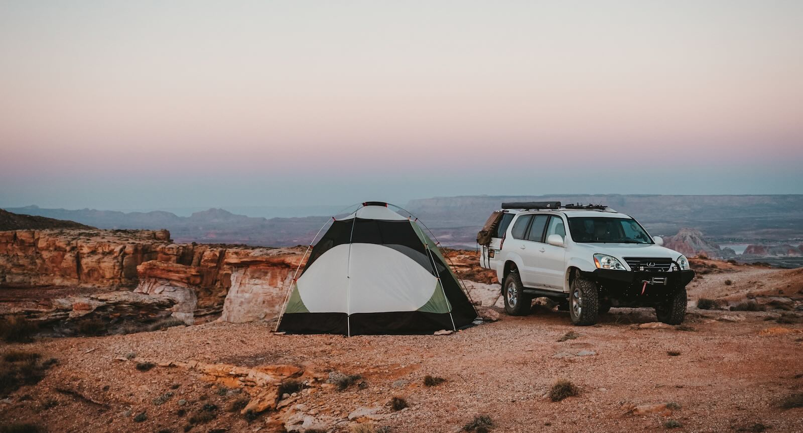 Classic white Lexus GX SUV parked off-road in a desert, a tent set up nearby.