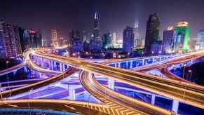 Highway overpasses above a city full of purple street lights, skyscrapers visible in the background.