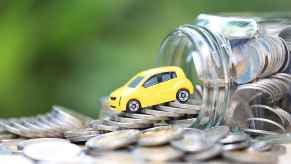 A toy car perched on an overturned jar of silver coins depiction of car insurance costs