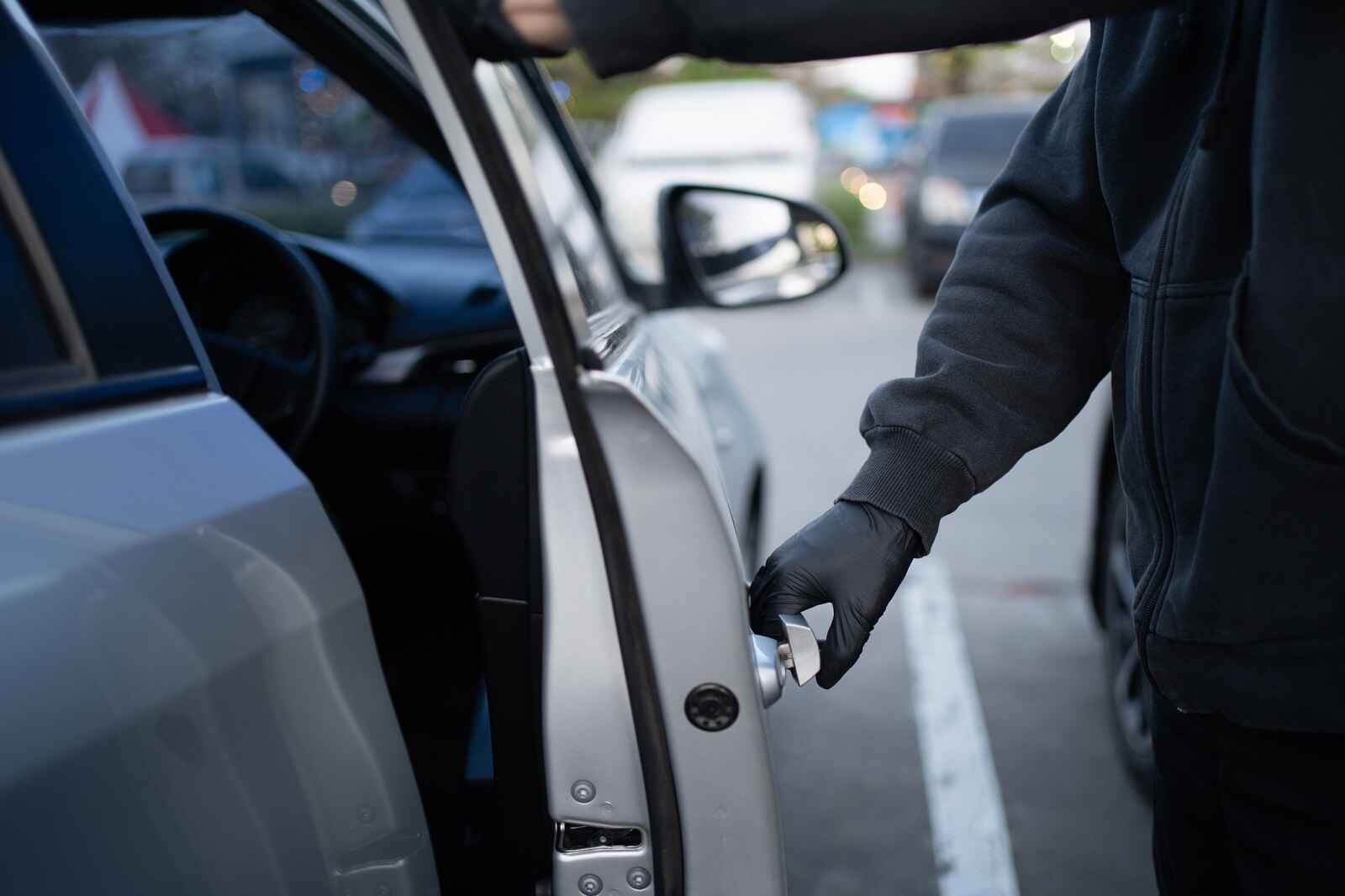 A man's gloved hand wearing black clothes opening a silver car door depiction of car getting stolen