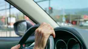 An elderly driver hands shown in close view gripping a car's steering wheel