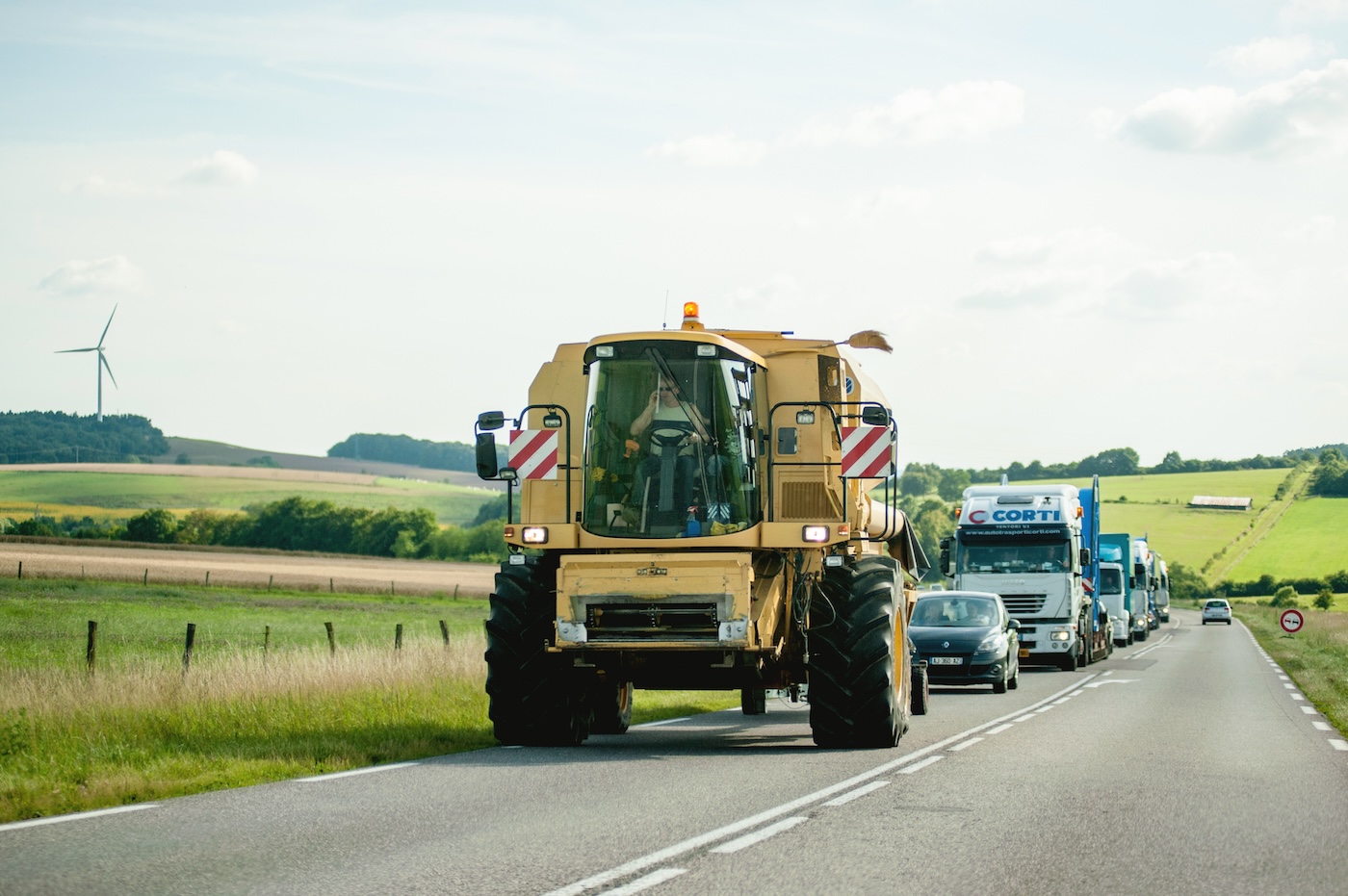 A man driving a tractor on the road with traffic behind 