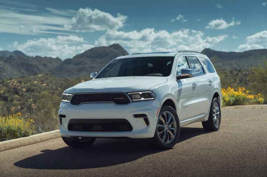 A white 2024 Dodge Durango SUV parked in left front angle view in front of mountains and cloudy blue sky