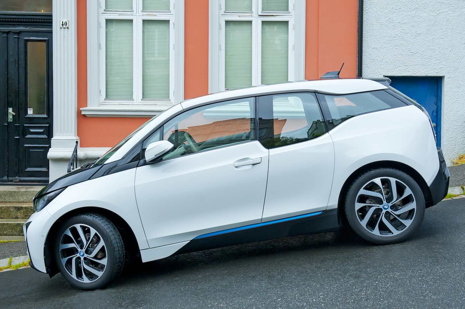 White BMW crossover EV parked on a steep street, houses visible in the background.
