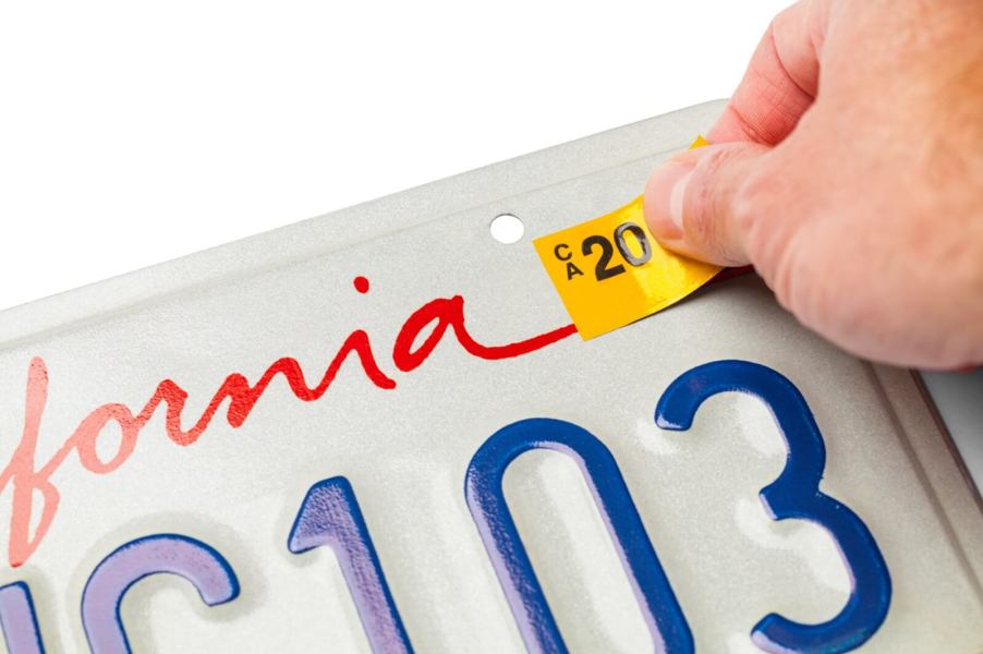 A motorist replaces the sticker on their license plate after fixing their expired registration.