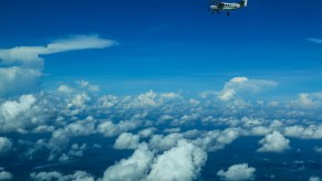 Tiny one-prop airplane flying through the sky, fluffy clouds below.