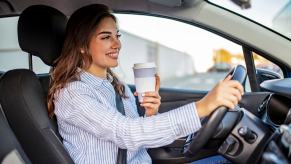 Woman holds a white to-go coffee cup while driving a car.
