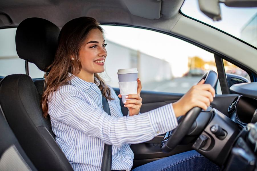 Woman holds a white to-go coffee cup while driving a car.