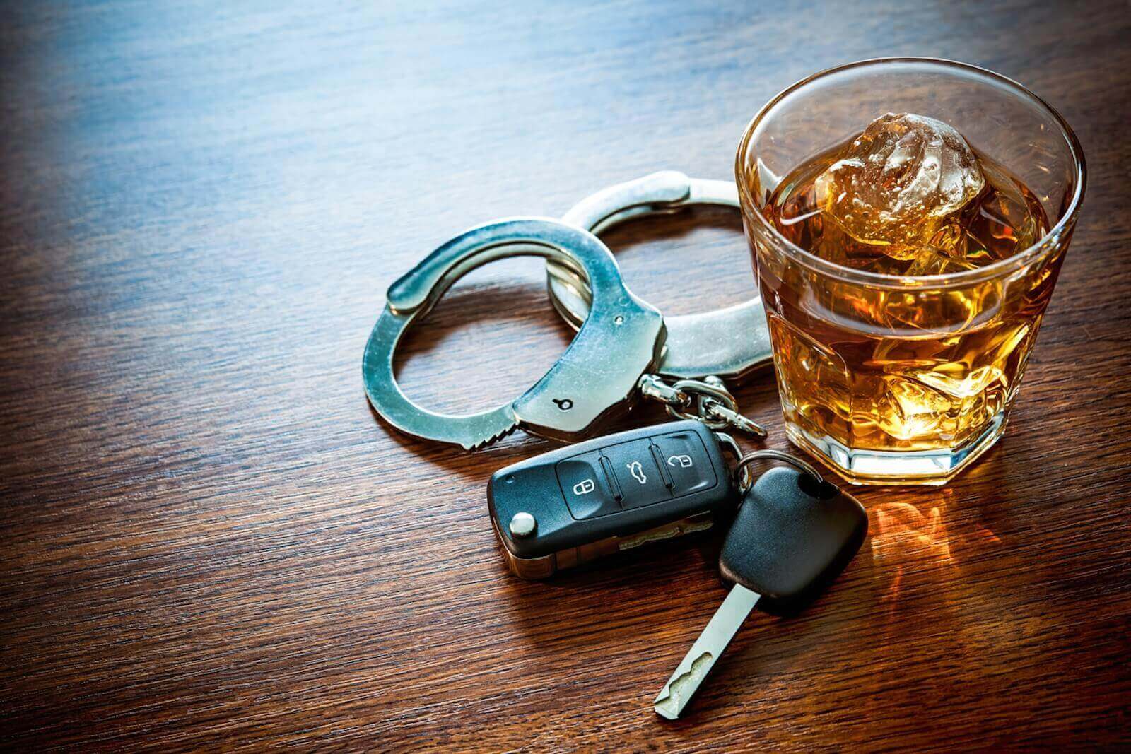 A DUI arrest dramatization places handcuffs with a drink and car keys.