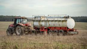 Red farm tractor pulling a metal tanker trailer through a pasture