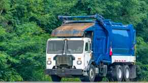 White and blue garbage truck driving on the road.
