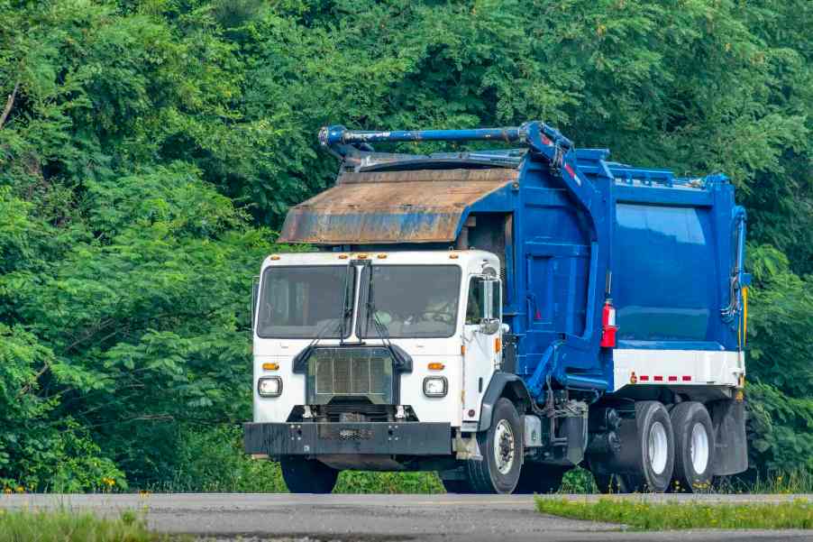 White and blue garbage truck driving on the road.