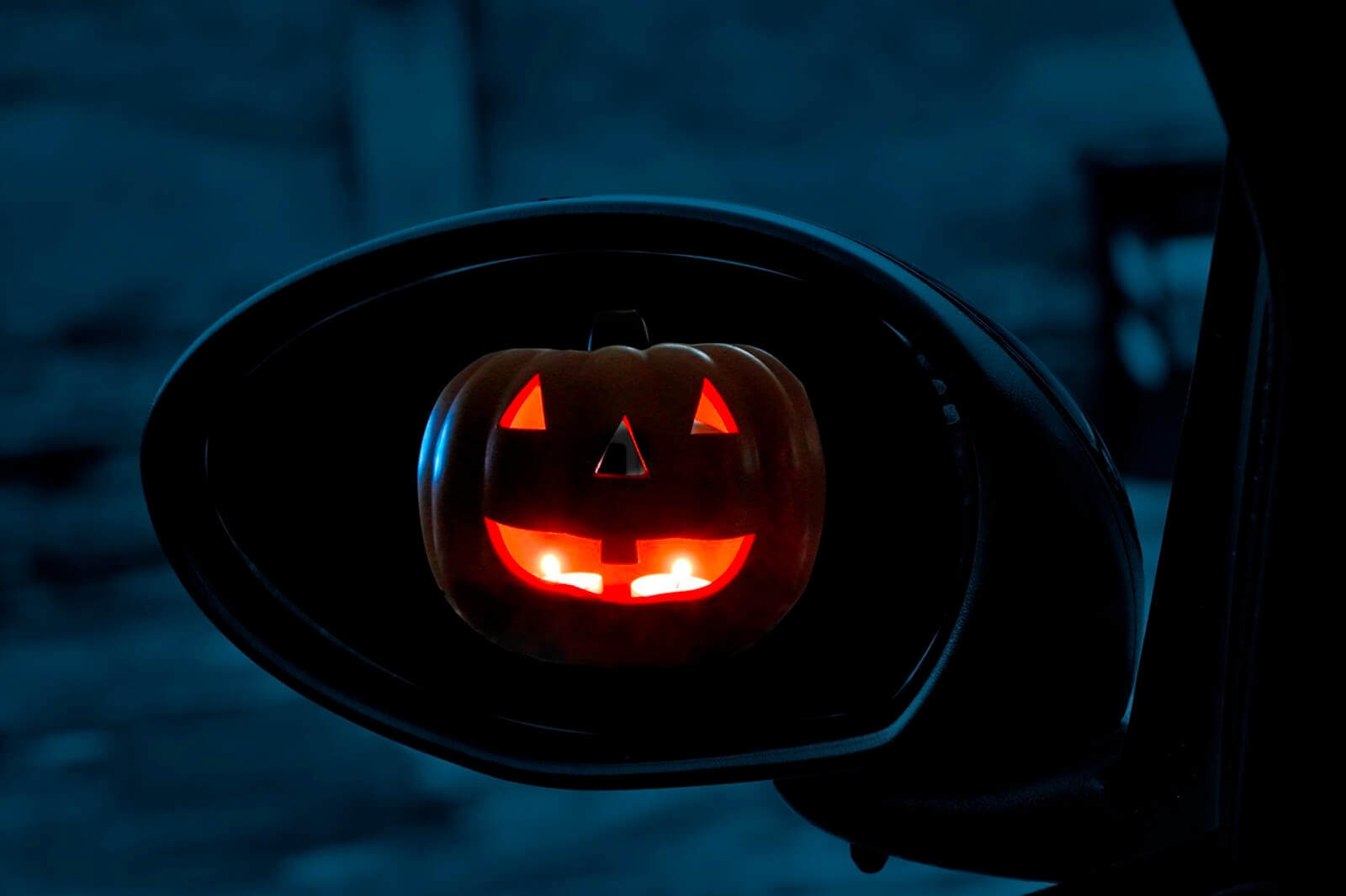 A Jack-o'-lantern, a symbol of Halloween, in a car's mirror.