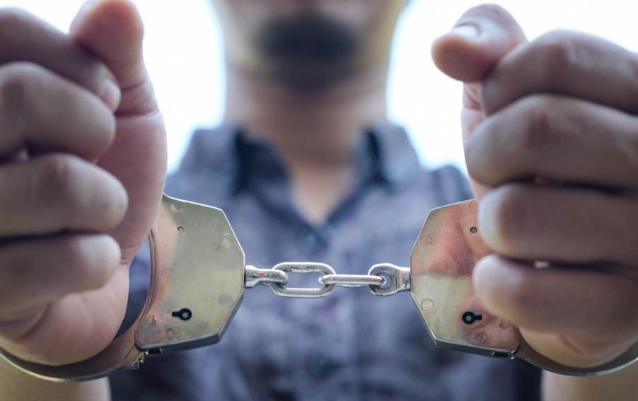 A car thief in handcuffs after police officers pulled him out of a stolen car.