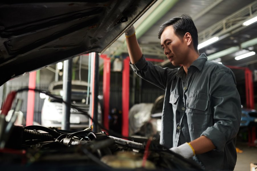 Mechanic stares at the engine compartment of a car with its hood up.