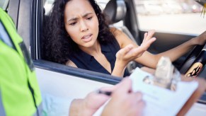 Driver watches a police officer filling out a ticket on a clipboard.