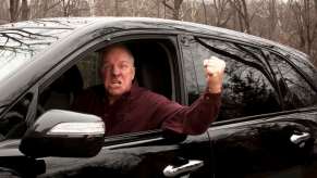 Gray-haired man in a black SUV raises a fist out of his car window during a road rage incident