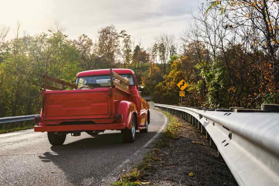 Red farm truck driving down the highway, trees visible in the background