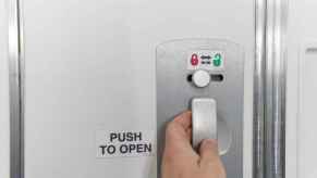 A man's hand operating the door lock on an airplane bathroom