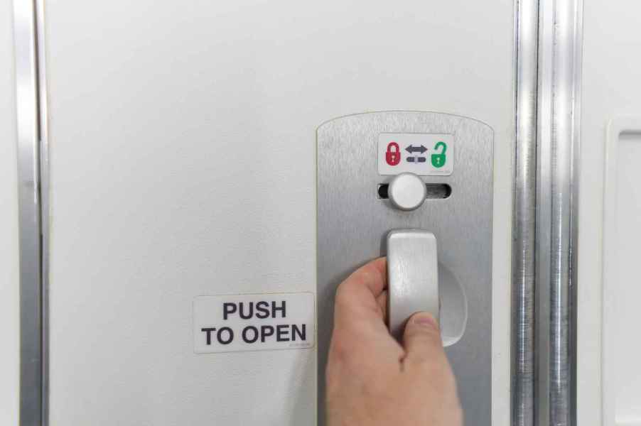 A man's hand operating the door lock on an airplane bathroom