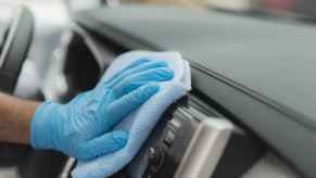 An interior car detail service with person's hand wearing a blue glove wiping car dash with blue microfiber towel in close view