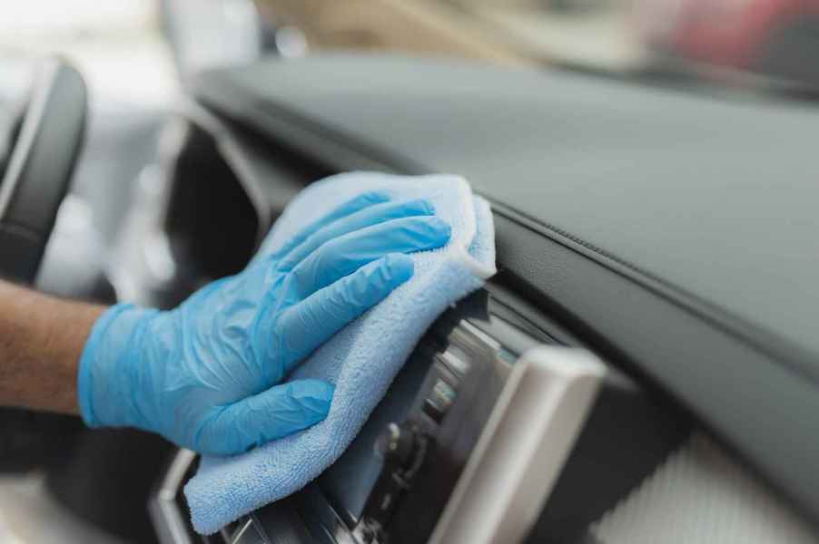 An interior car detail service with person's hand wearing a blue glove wiping car dash with blue microfiber towel in close view