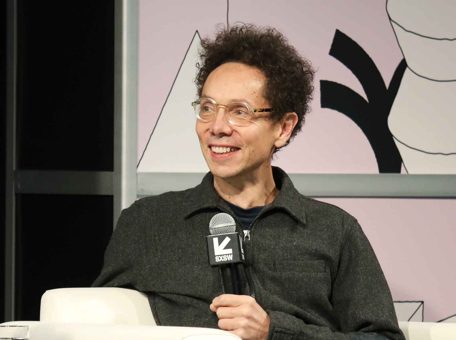 Malcolm Gladwell sitting and smiling at SXSW 2019 during a featured session on self-driving cars.
