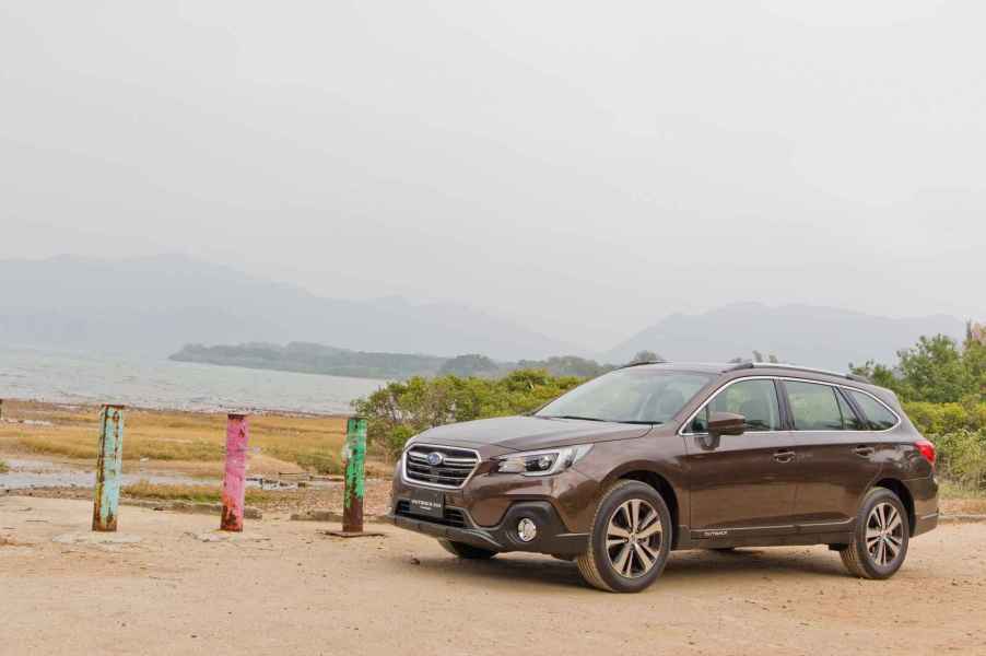 A dark brown Subaru Outback midsize SUV parked in left profile view at a Pacific Northwest-looking beach