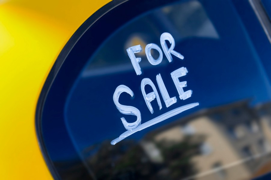 The words "For Sale" written in white chalk paint on the window of a used car for sale in close view