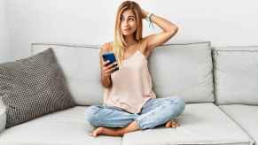 A woman sits on couch with cell phone confused expression depicting not understanding Instagram captions