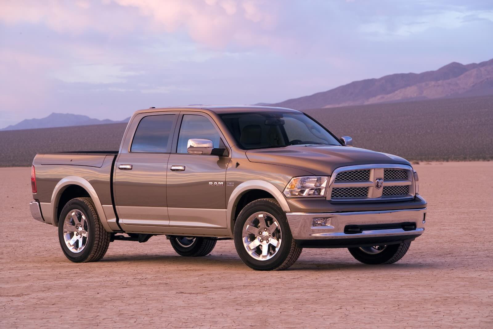 Quad cab Ram 1500 pickup truck parked on sand, mountains visible in the background.