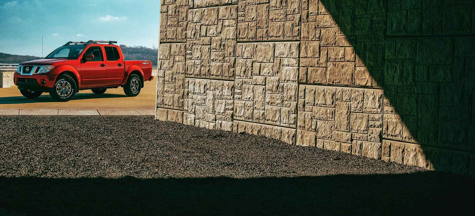 A red 2020 Nissan Frontier parked in background with stone wall in foreground