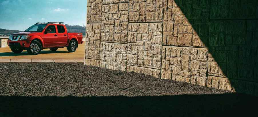 A red 2020 Nissan Frontier parked in background with stone wall in foreground