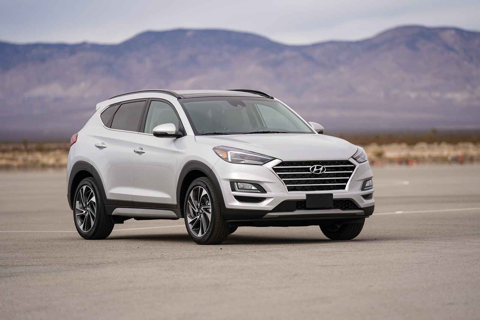 A white 2021 Hyundai Tucson parked on flat ground in front of a mountainous background in right front angle view.